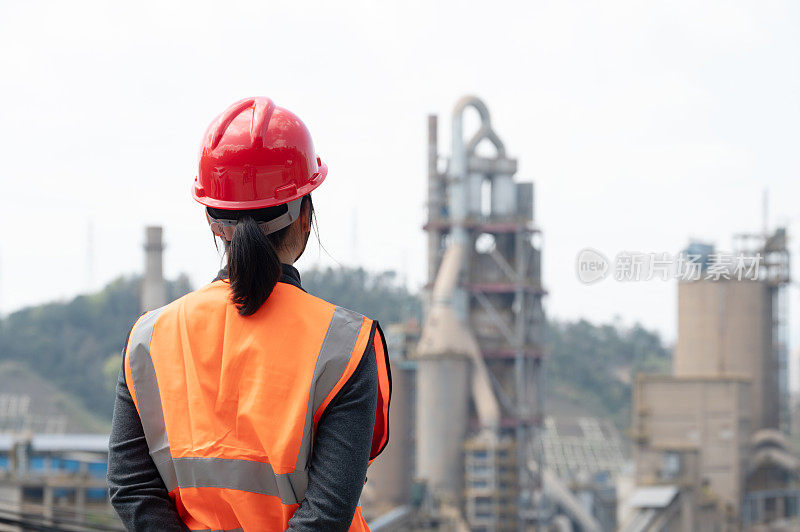 A female engineer looked at the cement factory in the distance with the camera on her back